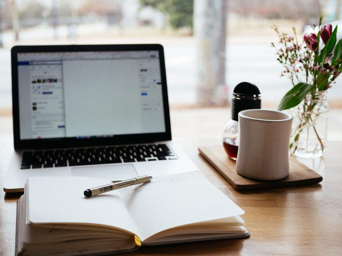 MacBook next to an open book on a wooden desk