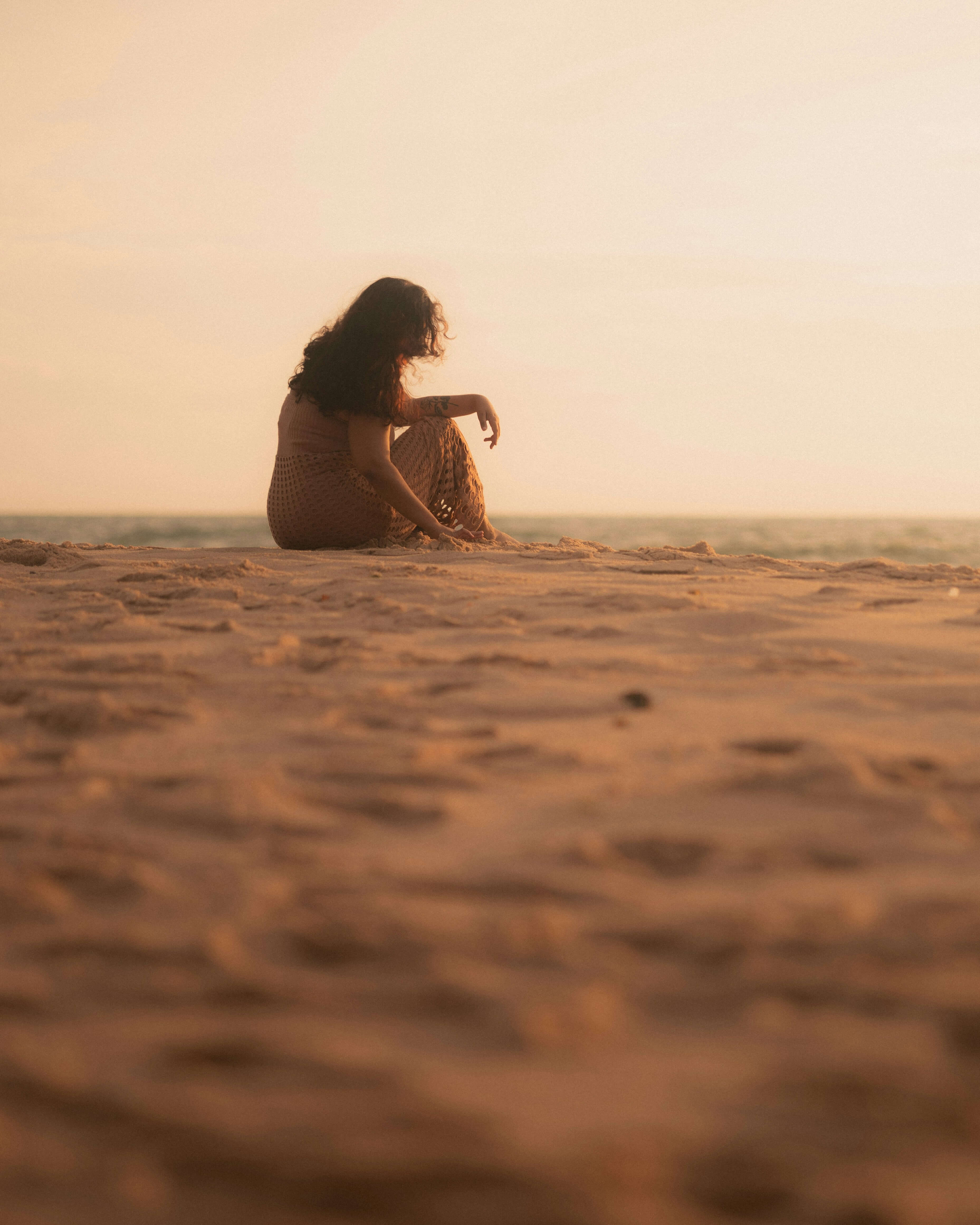 Woman sitting alone on a beach at sunset, contemplative mood